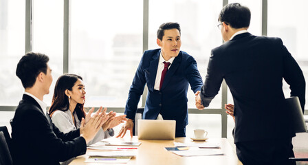 Image two asian business partners in elegant suit successful handshake together in front of group of casual business clapping hands in modern office.Partnership approval and thanks gesture concept