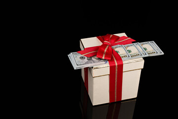 Caja de regalo y billetes de dólar americanos sobre fondo negro.