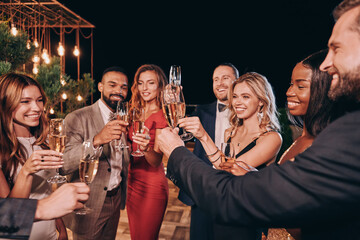 Group of beautiful people in formalwear toasting with champagne and smiling while spending time on...