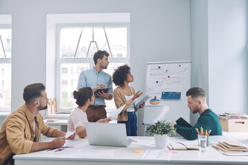 Group of confident young people in smart casual wear discussing business while having meeting in...