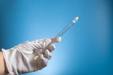 Linear halogen lamp with double base R7S. A gloved hand holds a lamp on a blue background.