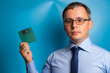 A man in a blue shirt, tie and glasses showing a green floppy disk. Retro technology concept.