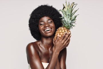 Portrait of beautiful young African woman holding pineapple and smiling