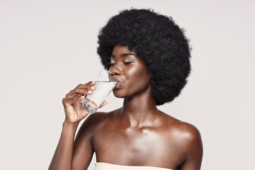 Portrait of beautiful young African woman drinking water while standing against gray background