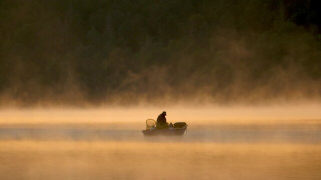 Morning fog on the lake at sunrise, man fishing from a boat, (Edersee, Germany)