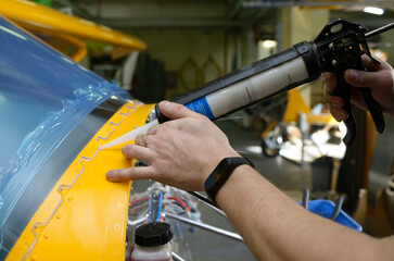 Fitter hands holding a glue gun fixing protective covering on the windscreen of the sport aircraft