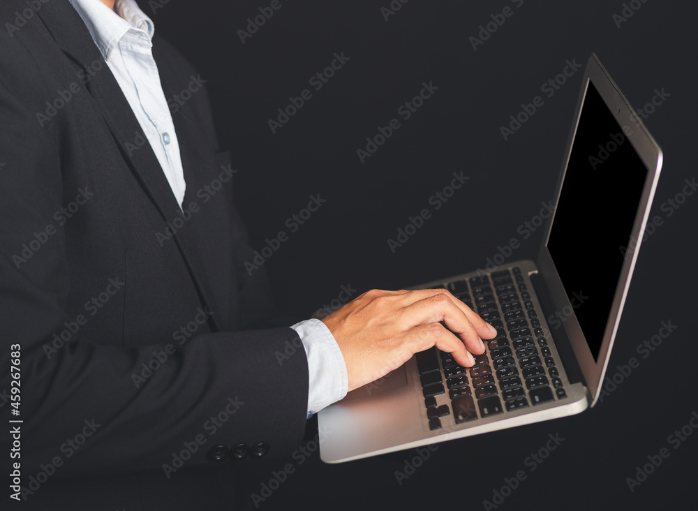 Poster midsection of a businessman in a suit holding and using a laptop while standing with black backgroun
