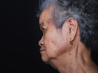 Side view of an elderly Asian woman with short gray hair and looking away while standing with a black background in the studio. Close-up photo. Aged people and health care concept