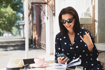 Beautiful stylish woman sitting in a street cafe drinking cappuccino and working on a laptop