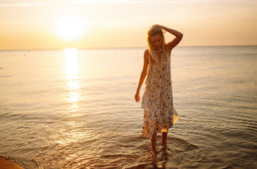 Fototapeta na wymiar Young woman walks along seashore at sunset. Travel, weekend, relax and lifestyle concept.