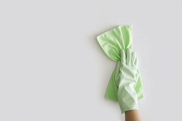 Hand with green rubber protective gloves holding rag and wipe up white table background. Cleaning service flat lay concept.