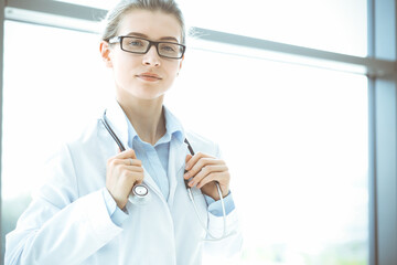 Beautiful woman doctor with stethoscope smiling charmingly and ready to help patients in the modern hospital. Medicine concept
