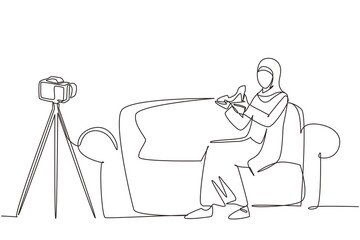 Single continuous line drawing Arabian beauty blogger is sitting at sofa, reviewing heels shoe in her hands while recording video with digital camera, tripod. One line draw design vector illustration