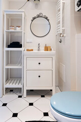 Small bathroom with stylish tiles on the floor, white cabinet, toilet and round mirror on the wall....