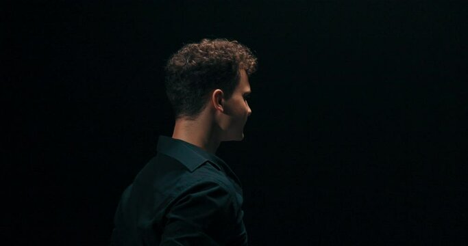 A professional experienced guy is dancing on a dark stage lit by a lamp, practicing new moves, poses, the man has black shirt unbuttoned, he is a choreographer, showing steps to beginner dancers