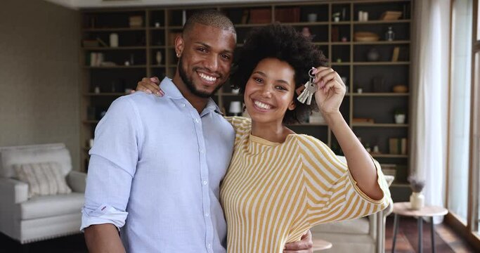 Happy homeowners African couple showing keys from their new house, first real-estate property, smile look at camera enjoy relocation day, new life starts. Bank loan, mortgage for young family concept