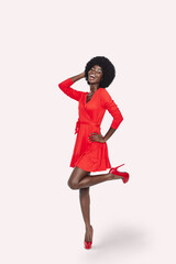 Full length of beautiful young African woman in red dress standing against gray background
