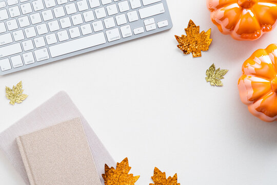 Autumn desk table with keyboard, notebooks, pumpkins, maple leaves on white background. Cozy home feminine workspace. Flat lay, top view.