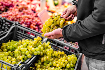 man hand holding grape in grocery store in supermarket
