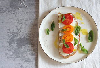 Sandwich with cheese, tomatoes and basil on a dessert plate. The top of the sandwich is watered with butter. Top view