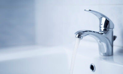 Water tap, stainless steel faucet. Water flow in bathroom with sink. Modern clean house interior. Hygiene concept.