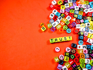 Colorful alphabet beads with text TRUST on red background.