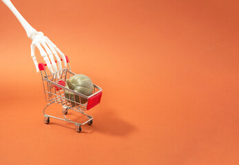 Skeleton hand is going back from Halloween shopping with pumpkin in shopping cart. Bizarre concept.