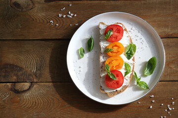 Sandwich with cheese, tomatoes and basil on a dessert plate. The plate stands on a wooden table. Sunny. Healthy food concept