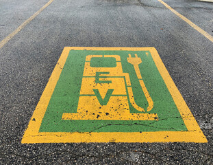 Green and yellow electric car parking symbol painted on slightly crumbling asphalt for EV charging. 