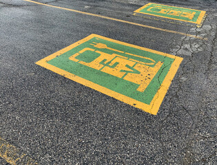 Green and yellow electric car parking symbol painted on slightly crumbling asphalt for EV charging. 