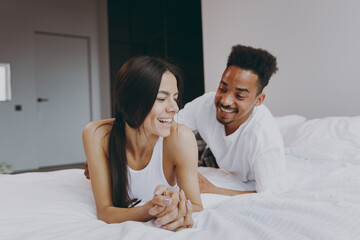Happy young couple two family in casual white clothes lying in bed on stomach man tickling woman...
