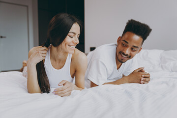 Happy young couple two man woman family in casual white clothes lying in bed on stomach flirting...