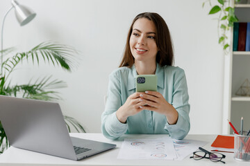 Young smiling minded successful employee business woman in blue shirt use hold mobile cell phone...