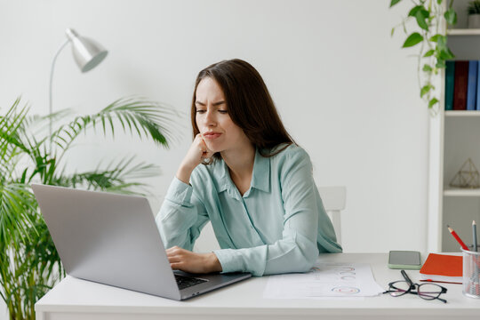 Young disappointed dissatisfied sad employee business woman in casual blue shirt sit work at workplace white desk with laptop pc computer at light modern office indoors. Achievement career concept.