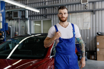 Strong serious confident young male professional technician car mechanic man in denim blue overalls...