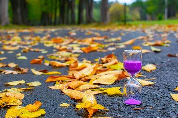sand pours in an hourglass as a symbol of the passing summer and the onset of autumn against the background of an asphalt path in a city park, square
