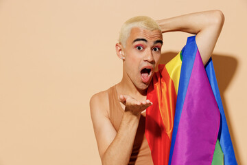 Young smiling happy sexy blond latin gay man with make up in beige tank shirt with rainbow flag on...