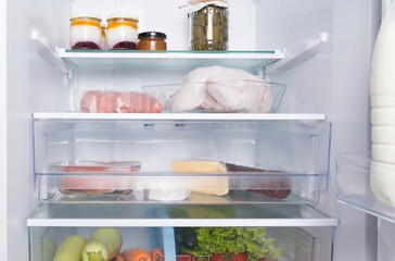 on glass shelves and drawers, in a white refrigerator, there are products, whole chicken, meat,...