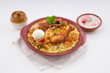 Chicken biryani , kerala style chicken dhum biriyani made using jeera rice and spices arranged in  earthen ware with raitha and lemon pickle as side dish on white background, isolated