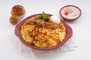 Chicken biryani , kerala style chicken dhum biriyani made using jeera rice and spices arranged in  earthen ware with raitha and lemon pickle as side dish on white background, isolated