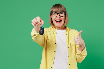 Elderly smiling happy caucasian woman 50s in glasses yellow shirt hold car keys fob keyless system...