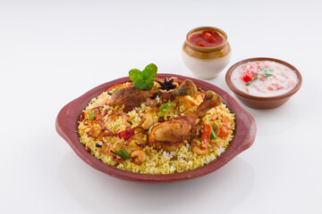 Chicken biriyani , kerala style chicken dhum biriyani made using jeera rice and spices arranged in  earthen ware with raitha and lemon pickle as side dish on white background, isolated
