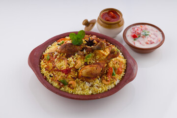 Chicken biriyani , kerala style chicken dhum biriyani made using jeera rice and spices arranged in  earthen ware with raitha and lemon pickle as side dish on white background, isolated