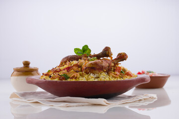 Chicken biriyani , kerala style chicken dhum biriyani made using jeera rice and spices arranged in  earthen ware with raitha and lemon pickle as side dish on white background, isolated