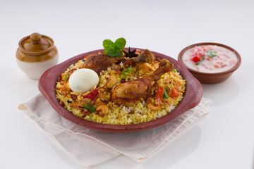 Chicken biryani , kerala style chicken dhum biriyani made using jeera rice and spices arranged in  earthen ware with raitha and lemon pickle as side dish on white background, isolated