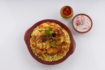 Chicken biriyani , kerala style chicken dhum biriyani made using jeera rice and spices arranged in  earthen ware with raitha and lemon pickle as side dish on white background, isolated