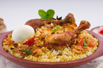 Chicken biryani , kerala style chicken dhum biriyani made using jeera rice and spices arranged in  earthen ware with raitha and lemon pickle as side dish on white background, isolated