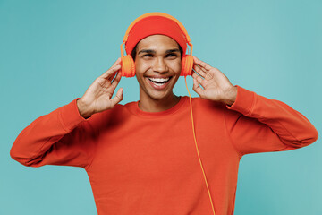 Young satisfied smiling fun happy african american man in orange shirt hat headphones listen to...