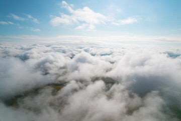Obraz premium Cumulus clouds, aerial background. Aerial shot with top view of white fluffy clouds gathering. In between the clouds the ground is visible here and there.