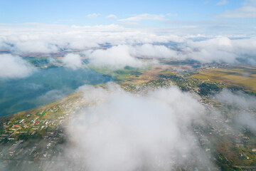 Cumulus clouds, aerial background. Aerial shot with top view of white fluffy clouds gathering. In between the clouds the ground is visible here and there.